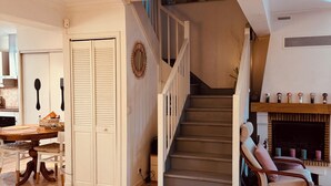 Un vaste salon agrémenté d’un escalier en bois, un coin repas avec une table et des chaises, et une cheminée décorée de divers objets.