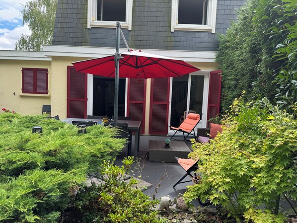 A patio area with a red umbrella, outdoor furniture, and lush greenery.