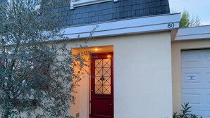 Une maison avec une porte rouge, un portail de garage et le numéro 80 sur le mur.