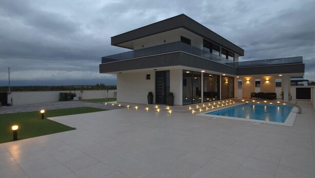 Una casa moderna de dos pisos con piscina, ventanas amplias y techo plano.