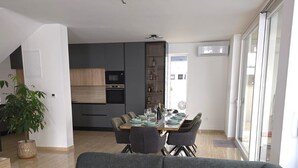Una sala de estar moderna con un sofá gris, un comedor con mesa de vidrio y una cocina al fondo.
