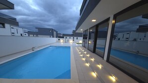 Una piscina moderna al aire libre con bordeado de baldosas e iluminación integrada, rodeada por un edificio de gran altura con ventanales amplios.