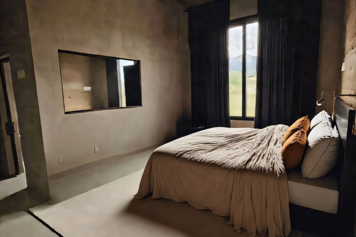 A bedroom with a bed, a window with curtains, a mirror, and a view of the outdoors.