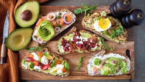 Una tabla de madera con varios sándwiches de aguacate sobre tostada.