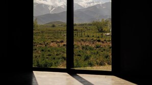 Habitación con un ventanal grande que ofrece vistas a un paisaje montañoso con picos nevados y un campo de vegetación escasa.