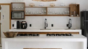A modern kitchen with a central island, built-in oven, and a hanging woven light fixture. - Vila Maremangue  (Porto Seguro)