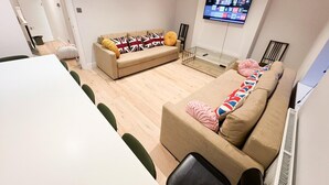 A modern living room with a sofa, a coffee table, and a TV mounted on the wall. - Stylish Penthouse in Willesden, Scrubs Lane (London)