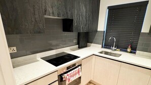A modern kitchen with a built-in oven, a sink, and a window with blinds. - Stylish Penthouse in Willesden, Scrubs Lane (London)