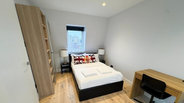 A bedroom with a bed, a desk, and a chair. There is a window with a view of buildings outside. - Stylish Penthouse in Willesden, Scrubs Lane (London)