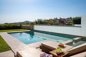 Ein Swimmingpool mit Liegestuhl und Tisch, auf dem sich ein Hut und Trauben befinden.