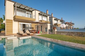 Ein modernes, zweistöckiges Haus mit Swimmingpool, Gartenmöbeln und einer Steinmauer.