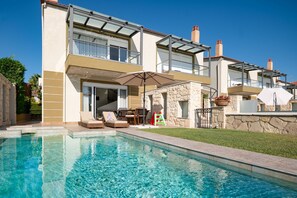 Ein modernes, zweistöckiges Haus mit Swimmingpool, Gartenmöbeln und einer Steinfassade.