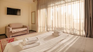 Ein Hotelzimmer mit Bett, einer Couch, einem Fernseher und großen Fenstern mit Vorhängen.
