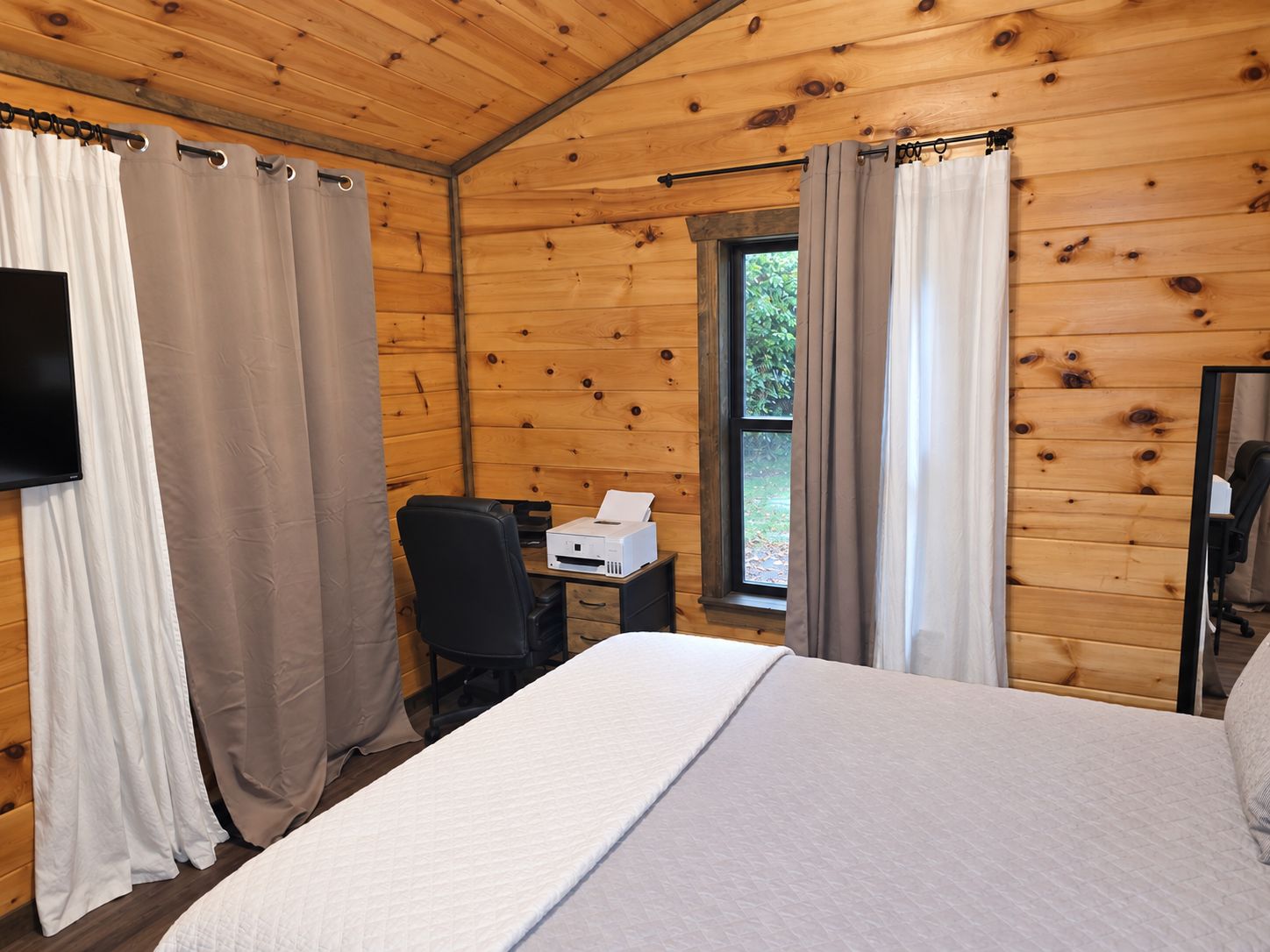 A wooden room with a bed, a desk, and a chair.