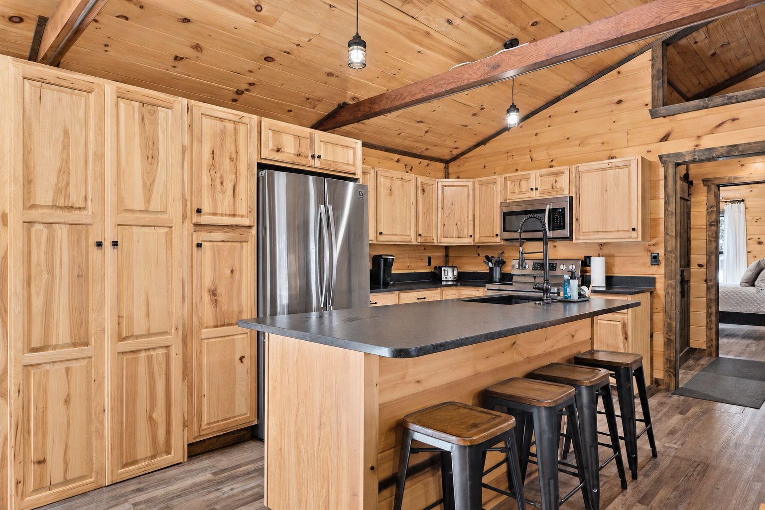 Interior de una cabaña de madera con una cocina que incluye un refrigerador de acero inoxidable, un microondas y una barra con taburetes.