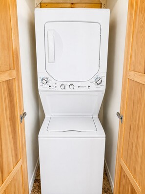 Lavadora blanca con mandos y puerta, ubicada entre dos puertas de madera.