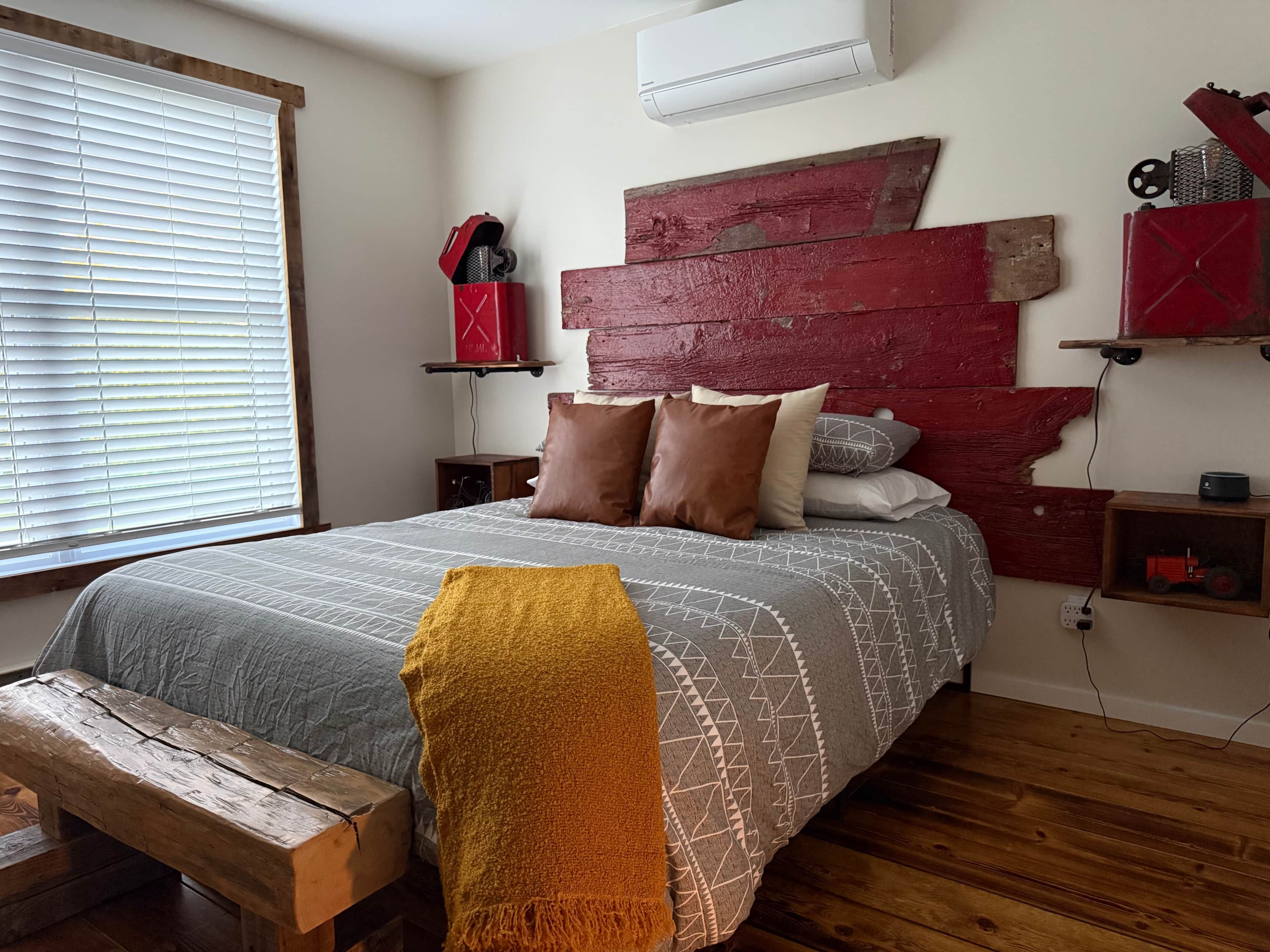A bedroom with a bed, wooden bench, pillows, a red headboard, and a shelf with a toy.