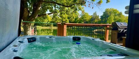 A hot tub with a wooden deck and a metal fence in the background.