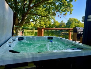 A hot tub with a wooden deck and a metal fence in the background. - Waterfront Nature Escape • Hot Tub (Tay Valley)