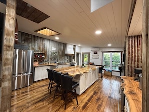 A modern kitchen with a central island, wooden flooring, and stainless steel appliances. - Waterfront Nature Escape • Hot Tub (Tay Valley)