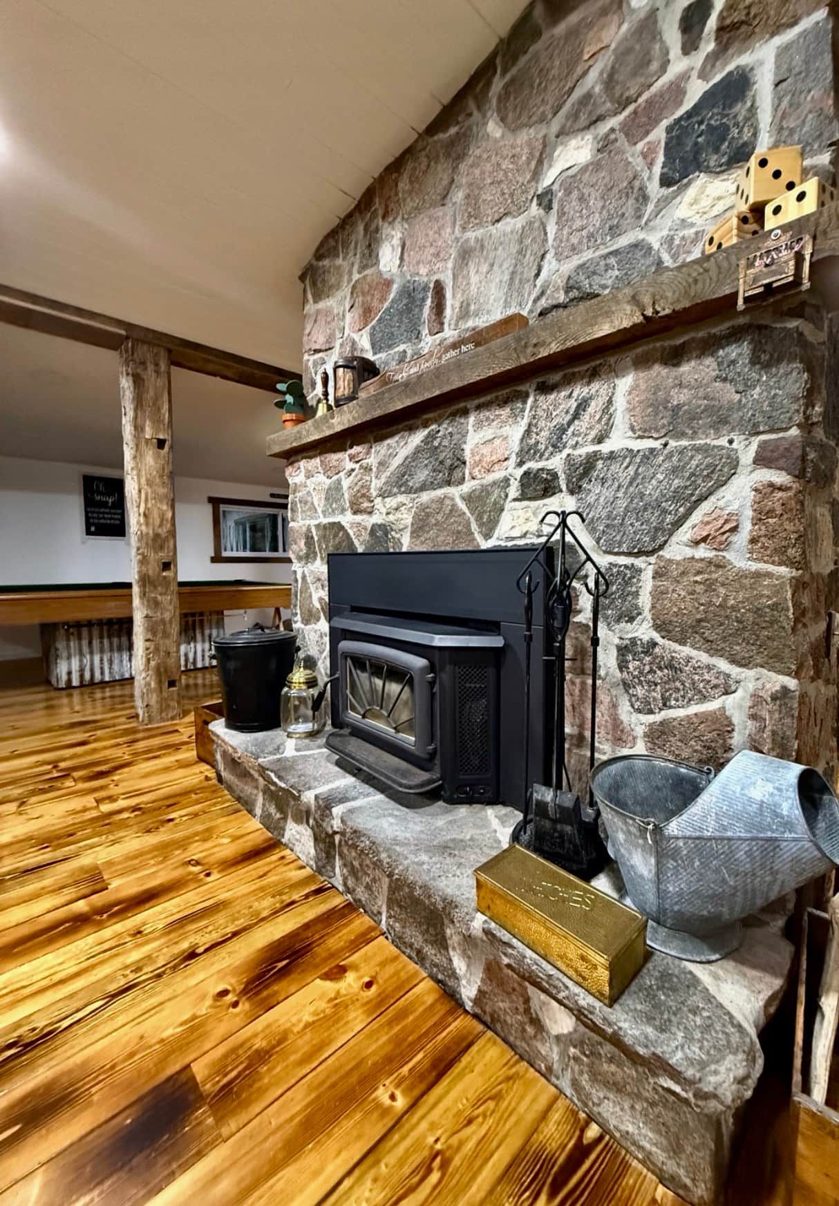 A stone fireplace with a black wood-burning stove, a metal bucket, and a brass plaque.