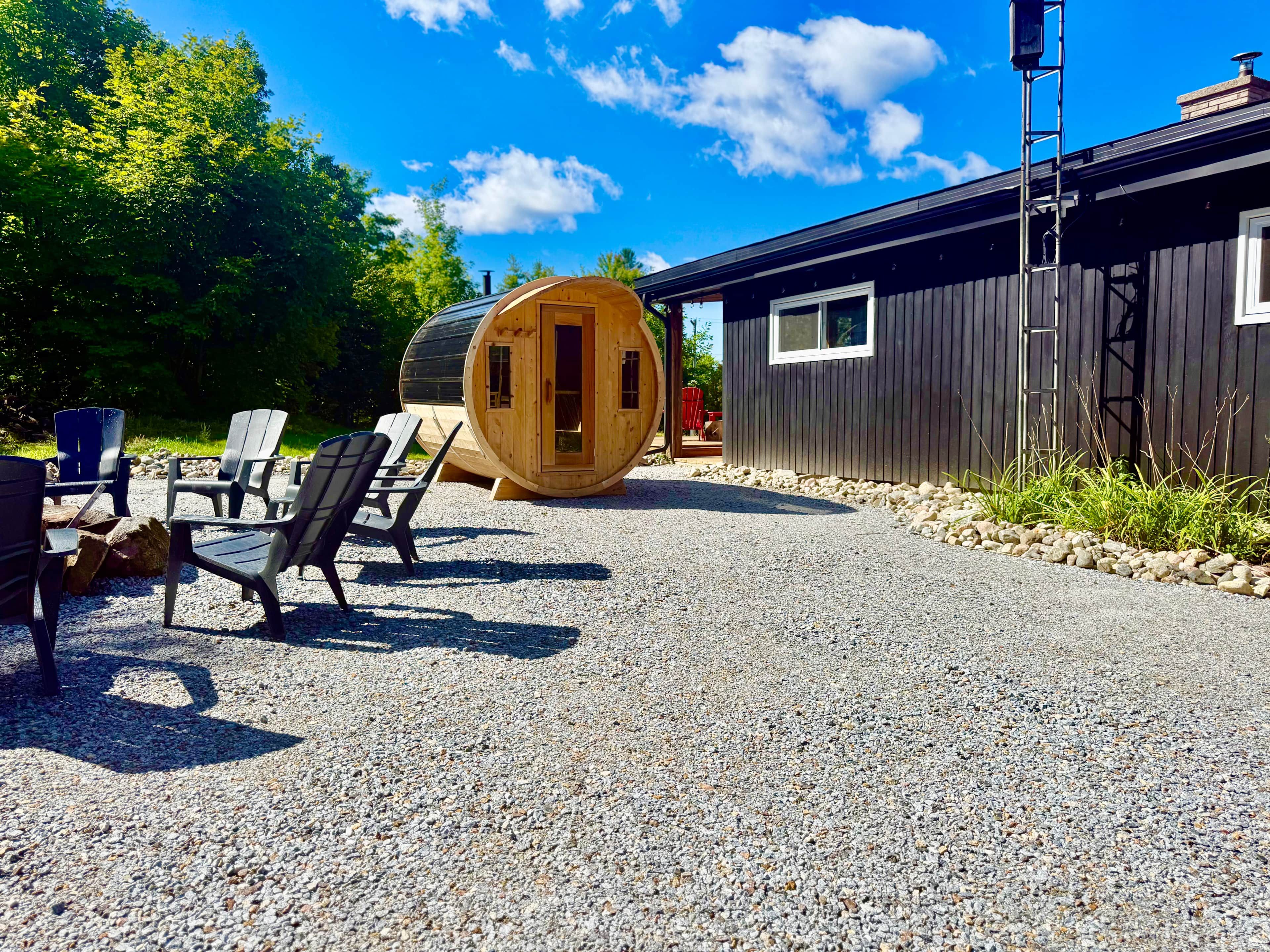 Un bâtiment en forme de tonneau, fait de bois, avec une allée en gravier et des sièges à l’extérieur.