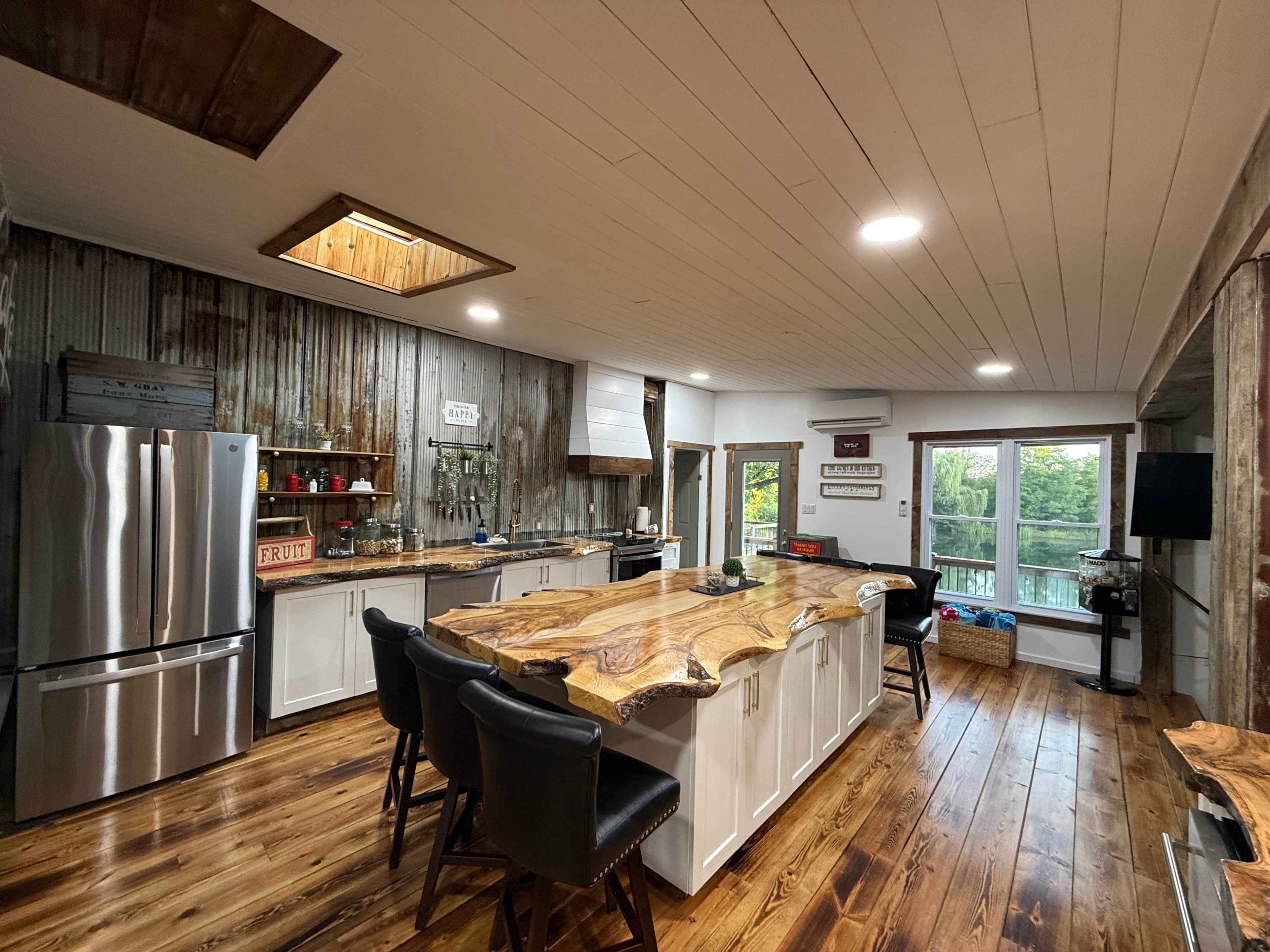 A modern kitchen with a central island, stainless steel appliances, and a rustic wooden ceiling.