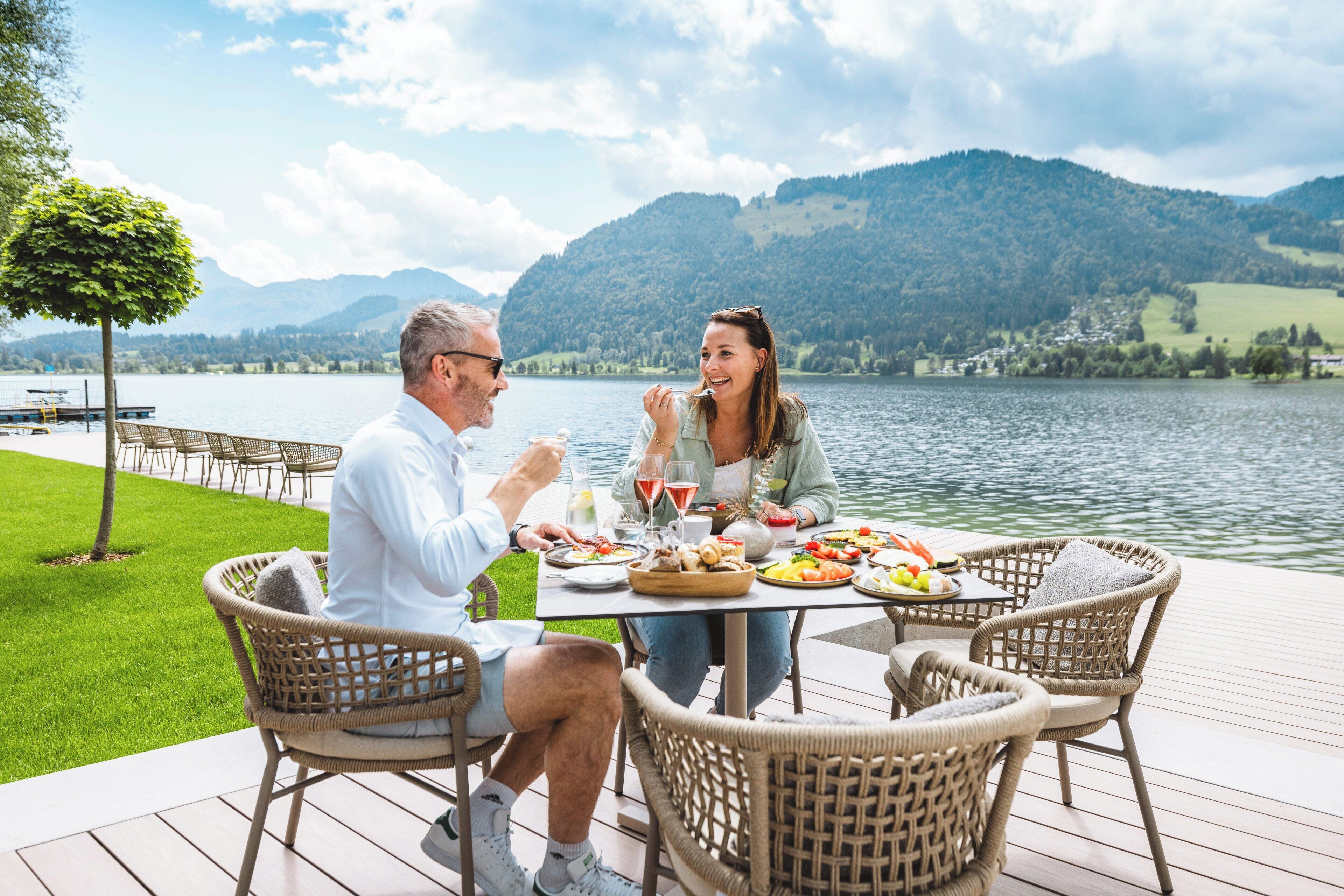 A couple dining at a table with a view of a lake and mountains.