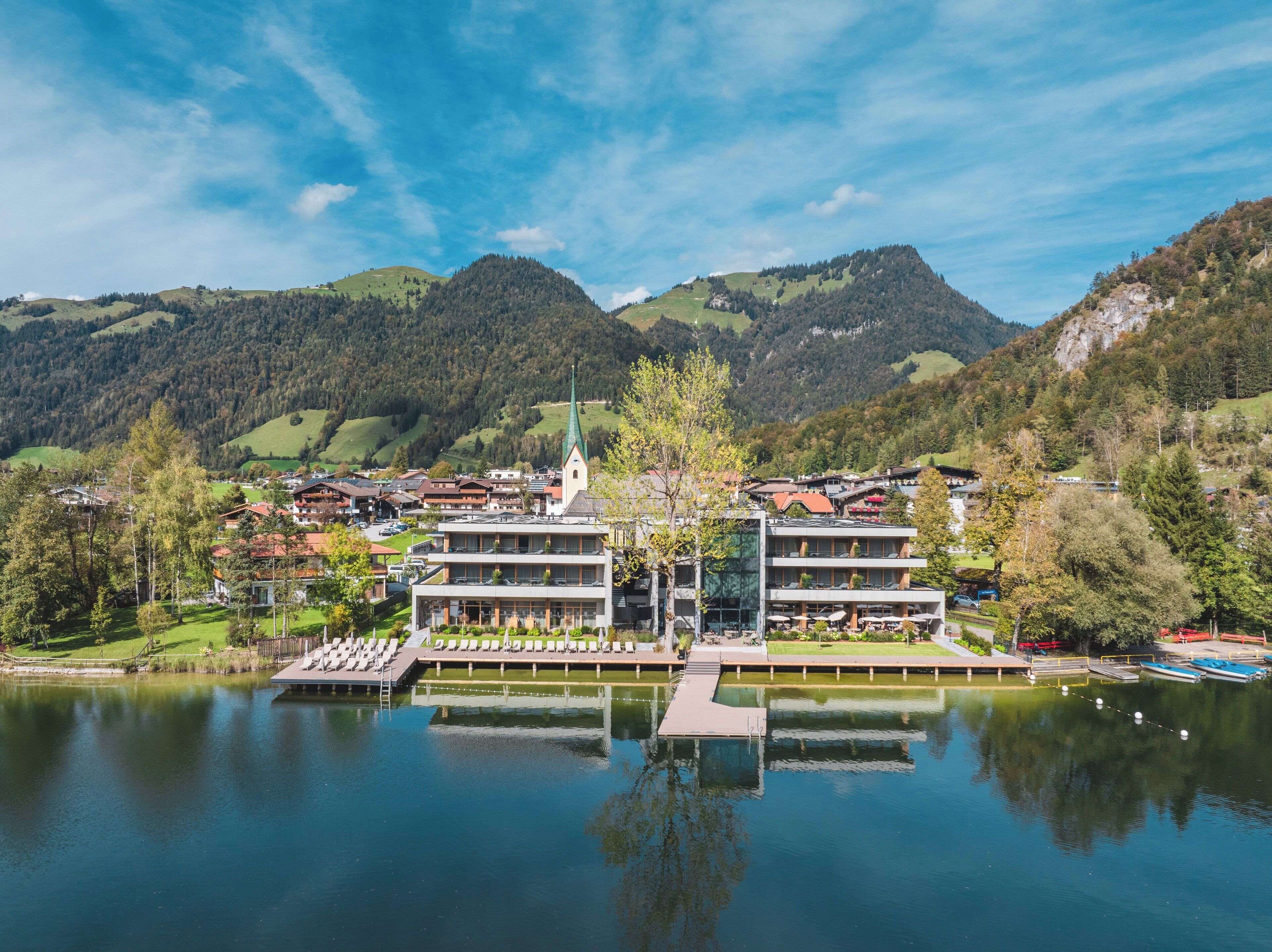 A lakeside hotel with a modern design, featuring a central building with multiple floors and a dock extending into the water.