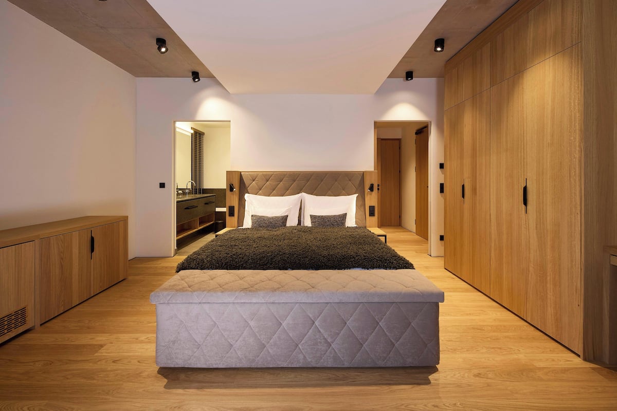 A modern bedroom with a large bed, wooden wardrobe, and a built-in bench.