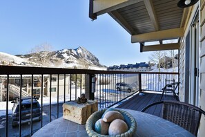 Un balcone con un tavolo in pietra, una sedia in vimini e vista su una montagna e auto parcheggiate.