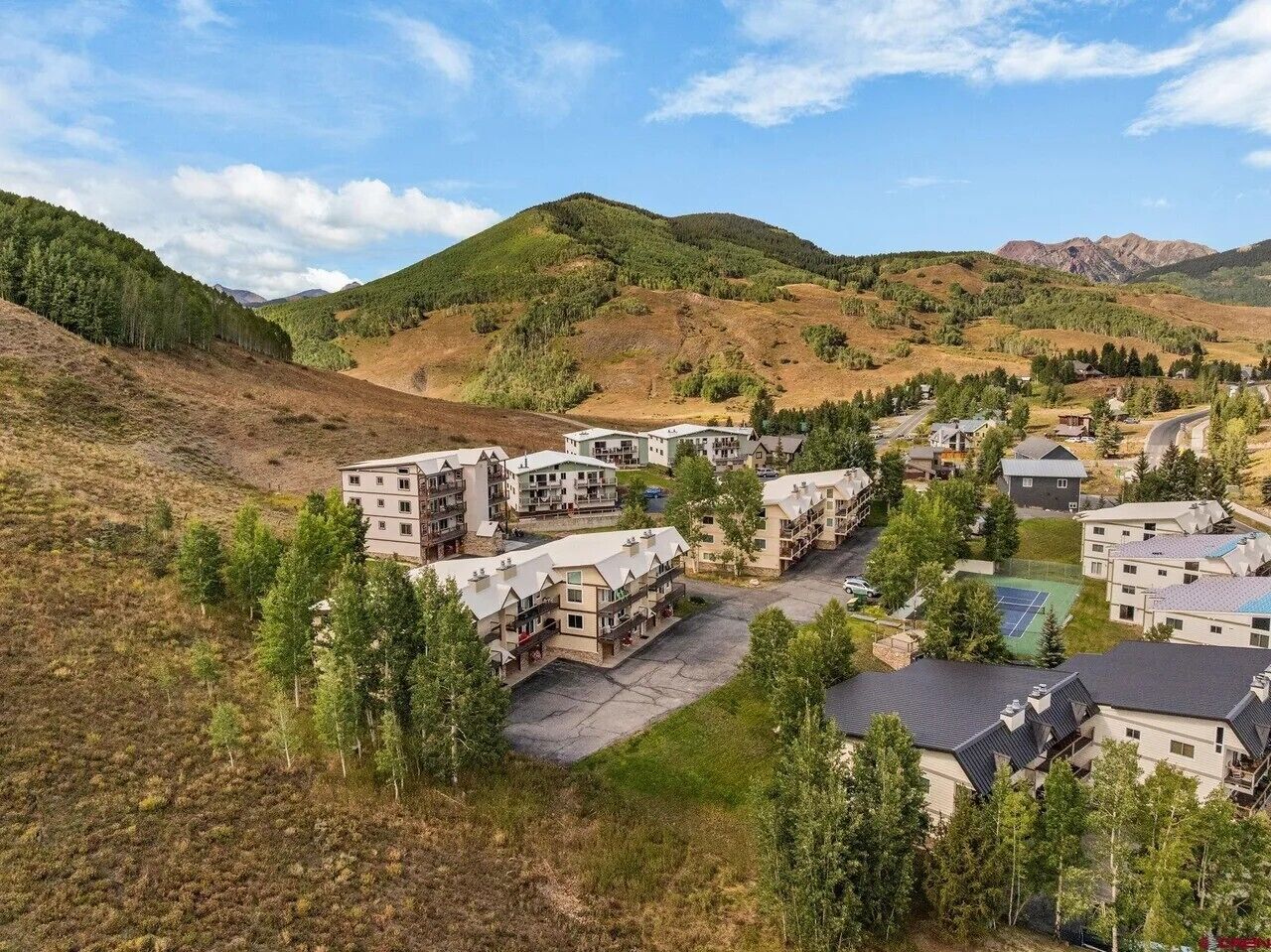 Zona residencial con varios edificios de dos pisos, una cancha de tenis y montañas al fondo.