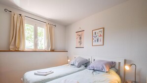 Een slaapkamer met twee bedden, een raam met gordijnen, een bedlampje en wanddecoratie.