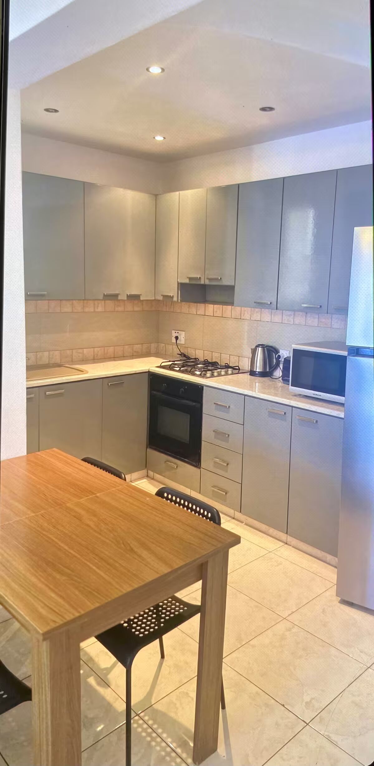 A modern kitchen with grey cabinets, a wooden dining table, and a built-in oven.