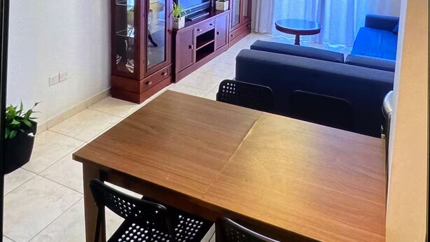 Une chambre d’hôtel avec une table à manger en bois, deux chaises noires, un téléviseur, un meuble, un canapé et un lustre.
