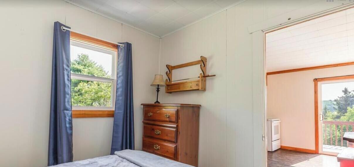 Een slaapkamer met een bed, een dressoir, een raam met gordijnen, een lamp en uitzicht op de omgeving.