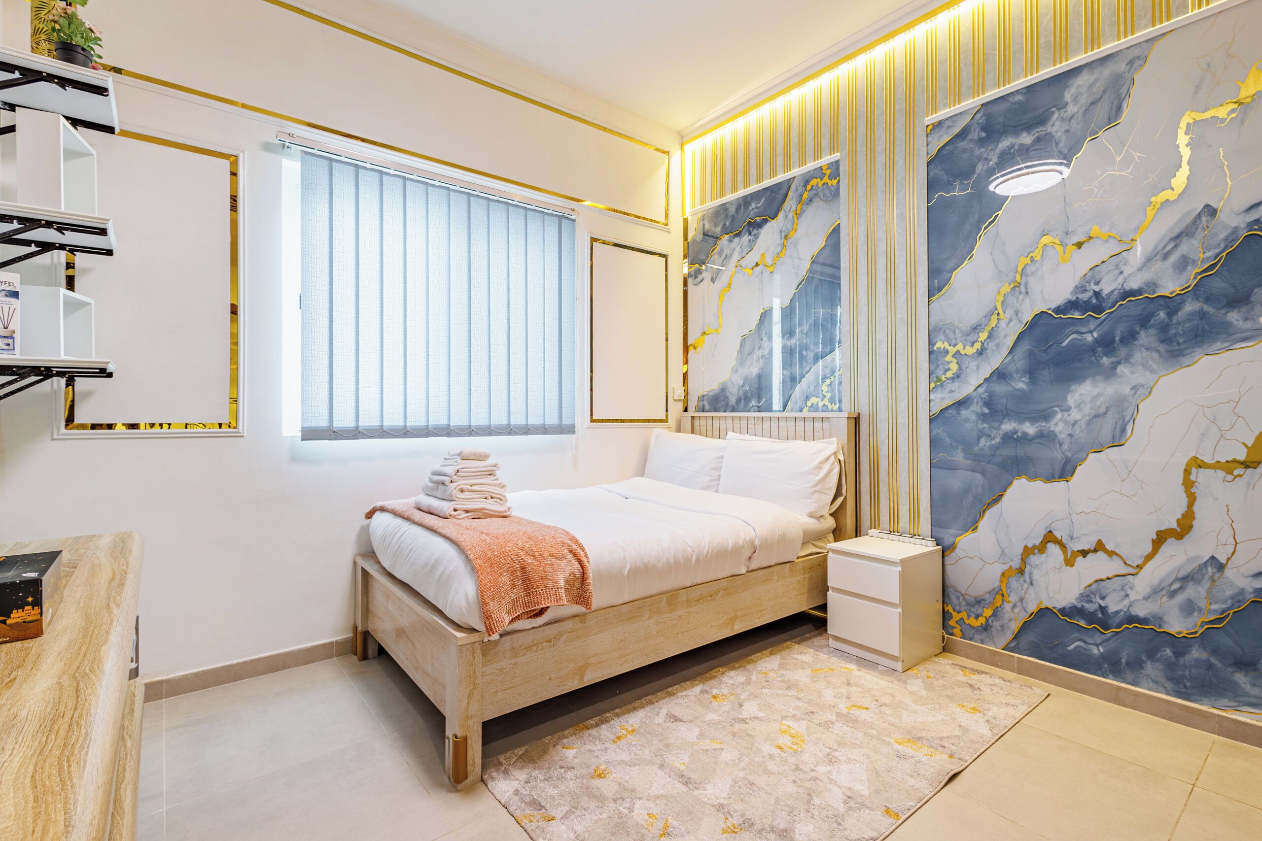 A modern bedroom with a wooden bed, a nightstand, a large marble wall, and a window with blinds.