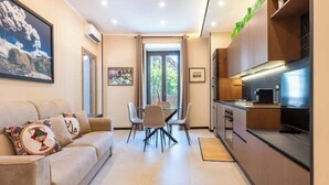 Una sala de estar moderna con un sofá, una mesa de comedor con sillas y una zona de cocina con armarios y electrodomésticos.