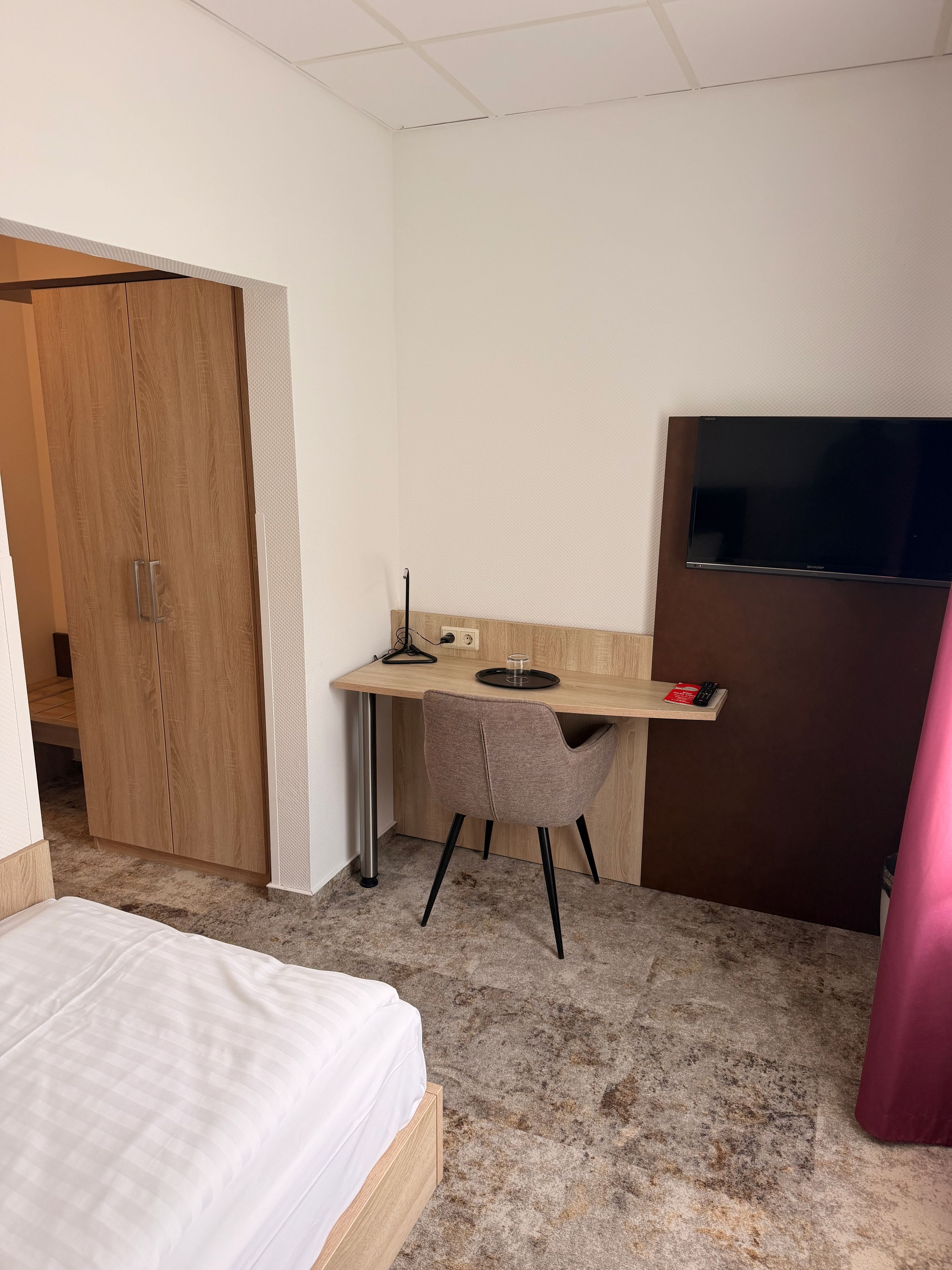 A hotel room with a bed, a desk with a chair, a TV, and a wardrobe.