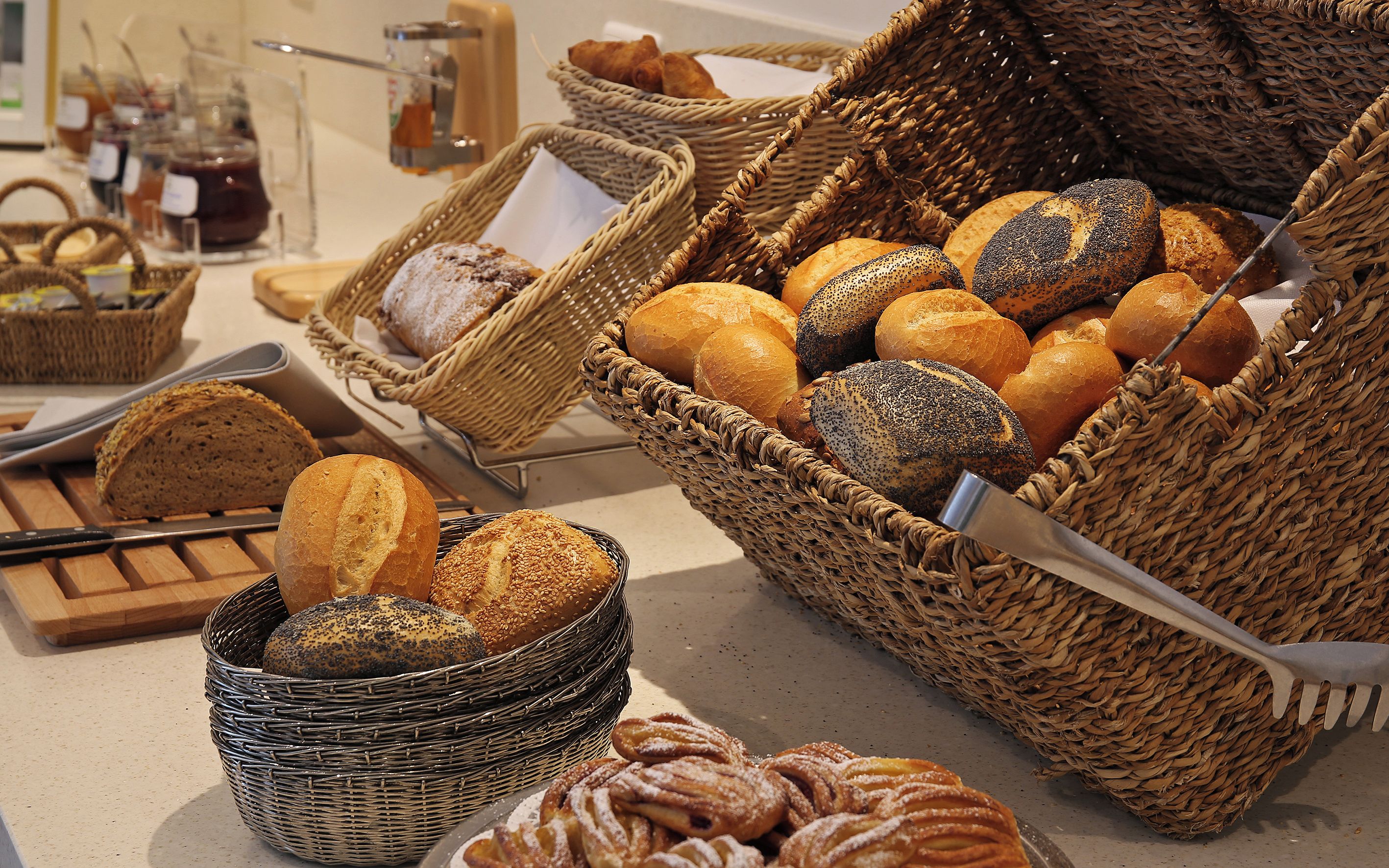 A variety of breads and pastries displayed in wicker baskets on a countertop.