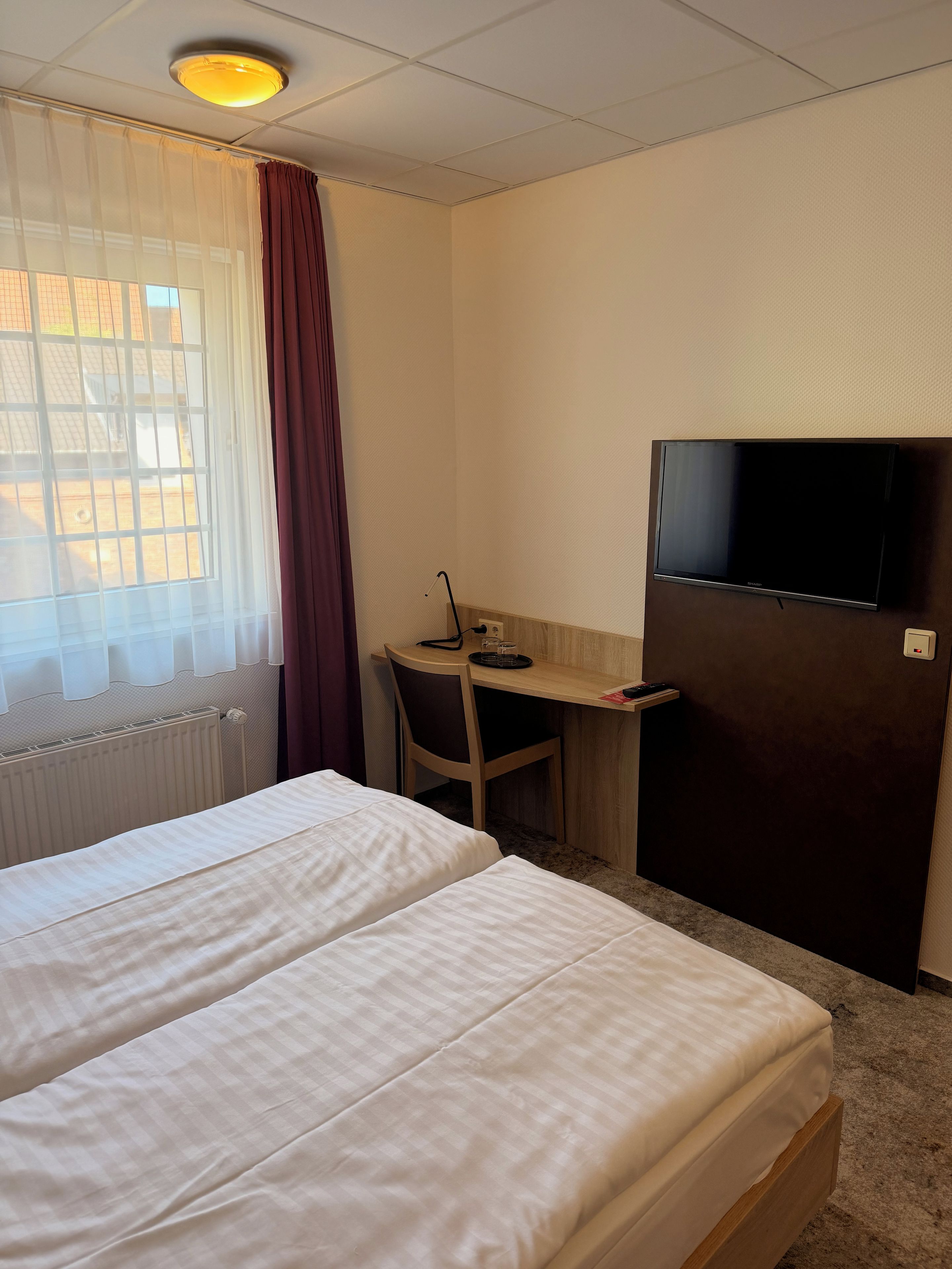 Habitación de hotel con dos camas, un escritorio con silla, televisión y ventana con cortinas.