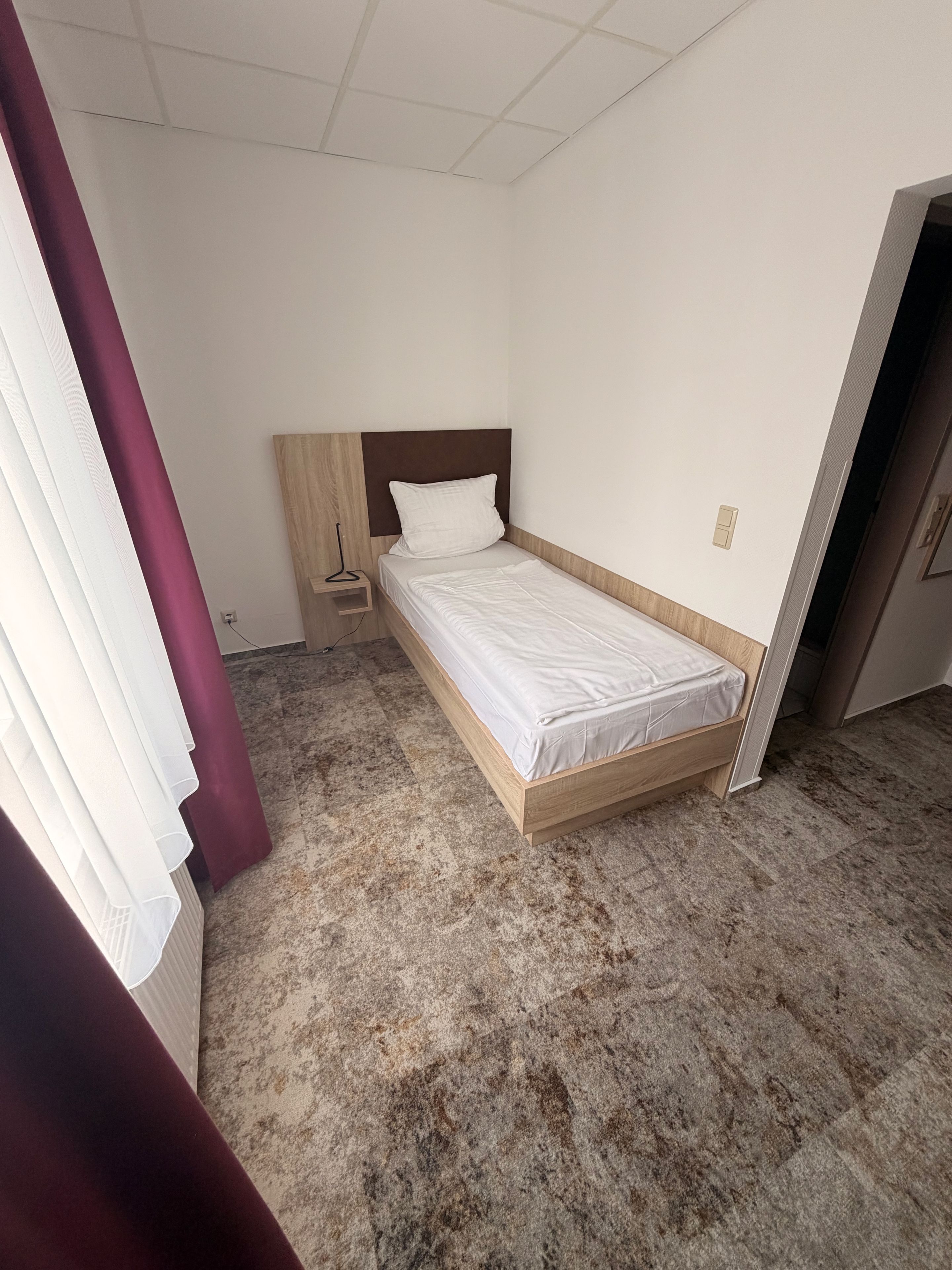 Een eenpersoonsbed met een houten hoofdeinde in een kamer met een betegelde vloer.