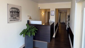 A hotel reception desk with a framed picture of a building, a potted plant, and a reception area with a desk and chairs. - Hotel Stadt Kamen (Kamen)