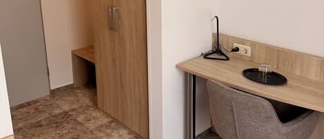 Una habitación compacta con un armario de madera, un escritorio con una silla y una mesita con un vaso.