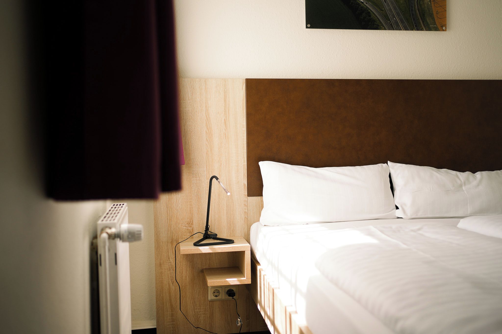 A hotel room with a bed, a nightstand, a lamp, and a radiator.