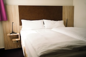 A neatly made bed with white linens, a wooden headboard, and a bedside table with a lamp. - Hotel Stadt Kamen (Kamen)