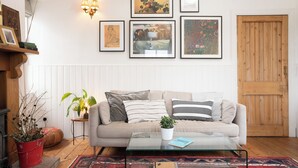 Ein gemütliches Wohnzimmer mit einem beigen Sofa, einem Glastisch und einem topfgestellten, roten Pflanzen.