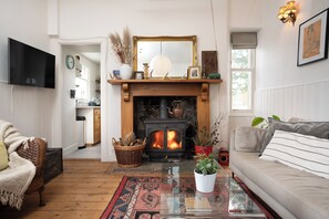 Una sala de estar con chimenea, un sofá, un televisor y un rincón de comedor visible a través de una puerta abierta.