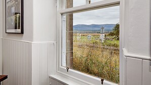 Ein Zimmer mit großem Fenster und Blick auf eine ländliche Landschaft mit Bergen im Hintergrund.