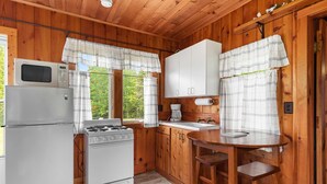 A compact kitchen with a refrigerator, stove, and white cabinets. - Million Dollar View | Lakefront Studio Cottage w/ Mackinac Bridge & Island Views (Cheboygan)